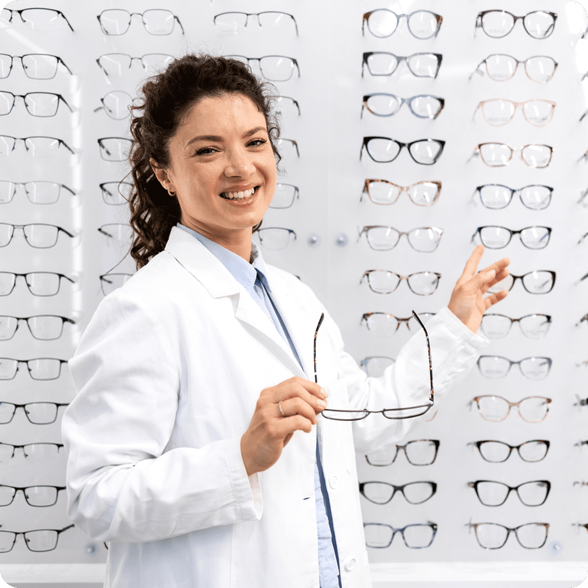 Optician smiling with eyeglasses display wall.