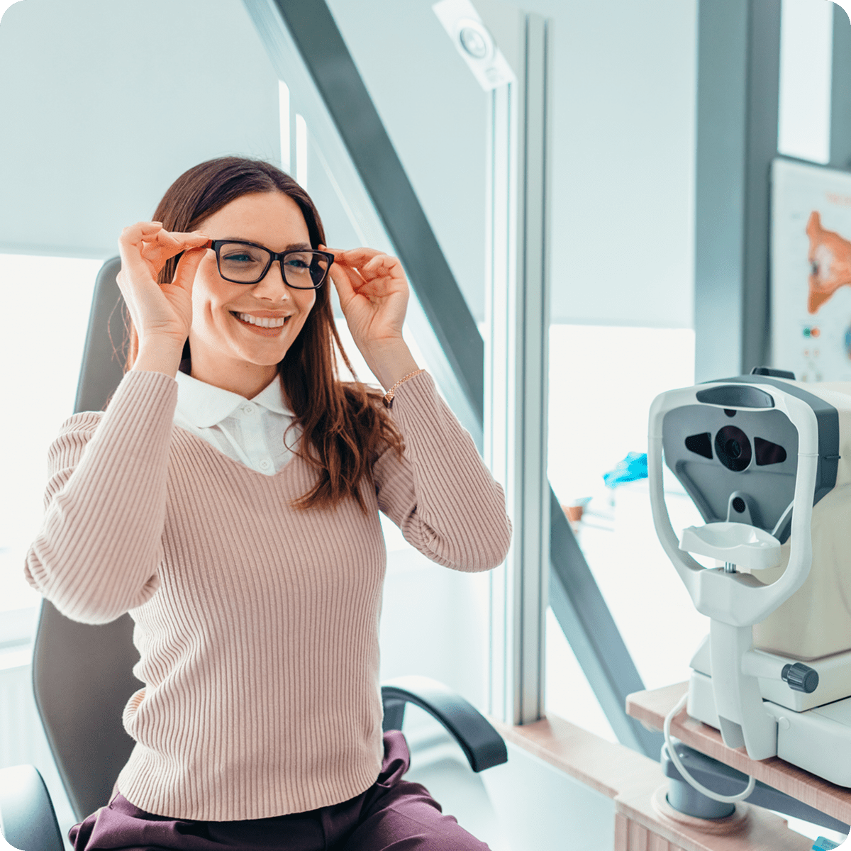 Woman adjusting glasses near eye examination equipment.